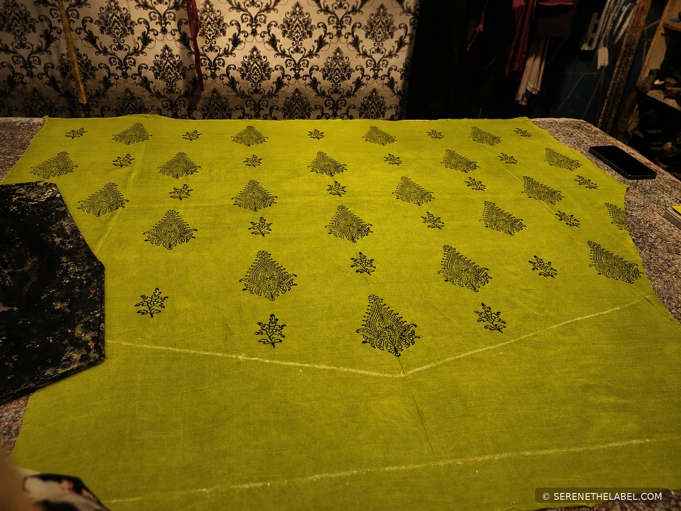 Green printed fabric laid out across a cutting table